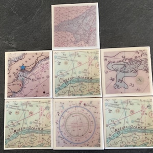 May include: Seven square ceramic tiles with nautical chart designs. The tiles feature various sections of nautical maps with blue, green, and pink hues. Some tiles display text like "HONSLAN" and "Middle-Ground".