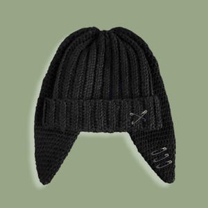 May include: Black knitted beanie with ear flaps and safety pins attached. The beanie has a ribbed texture and a rounded crown.