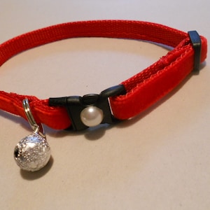 May include: Red velvet cat collar with a silver bell and a white pearl accent.