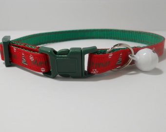 Könnte beinhalten: Ein rot-grünes Haustierhalsband mit einem sich wiederholenden Muster aus Weihnachtsbäumen, Schneeflocken und dem Text Merry Christmas. Es verfügt über eine dunkelgrüne Kunststoff-Steckschnalle, einen silbernen Metallring und eine weiße Glocke.