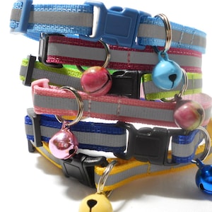 K&ouml;nnte beinhalten: Ein Stapel bunter Katzenhalsb&auml;nder mit reflektierenden Streifen und Gl&ouml;ckchen. Die Halsb&auml;nder sind in verschiedenen Farben wie Blau, Rosa, Gr&uuml;n und Gelb gehalten, jeweils mit passenden Kunststoffschnallen. Die Gl&ouml;ckchen sind in Blau-, Rosa- und Gelbt&ouml;nen gehalten.
