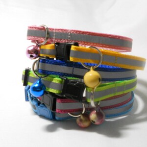 K&ouml;nnte beinhalten: Ein Stapel bunter Katzenhalsb&auml;nder mit reflektierenden Streifen und Gl&ouml;ckchen. Die Halsb&auml;nder sind in den Farben Rosa, Gelb, Blau und Gr&uuml;n gehalten, jeweils mit einer schwarzen Kunststoffschnalle. Die Gl&ouml;ckchen sind in verschiedenen Farben, darunter Rosa, Gelb und Blau.