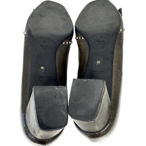 May include: Pair of metallic bronze-colored Prada heels, size 40, with block heels and studded accents. The soles are black with the Prada logo and "Made in Italy" text.