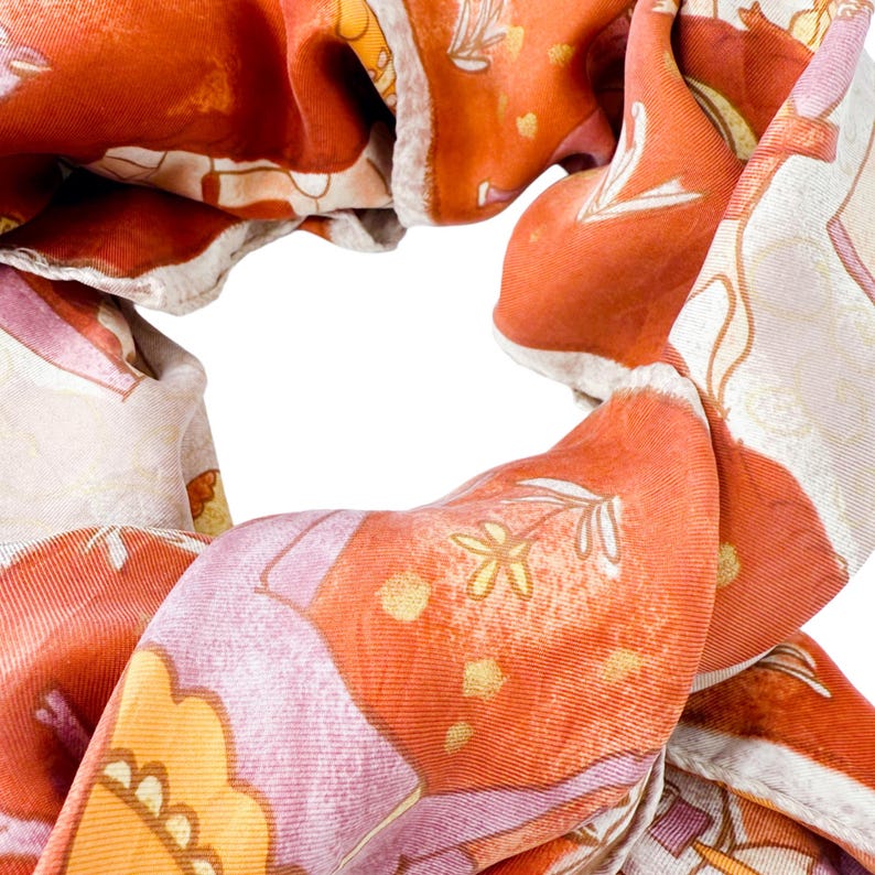 May include: A scarf featuring a vibrant orange and cream color palette with a repeating pattern of stylized flowers, leaves, and geometric shapes. The fabric has a smooth, slightly lustrous texture with visible woven lines throughout the material.