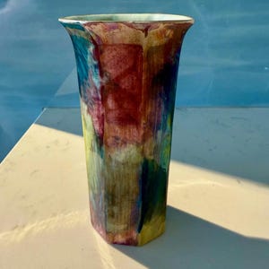 Peut inclure: Un vase en céramique multicolore de forme géométrique. Le vase est recouvert d'un glacis bleu clair, vert, jaune et rouge.
