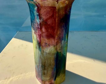 May include: A multi-colored ceramic vase with a geometric shape. The vase has a light blue, green, yellow, and red glaze.