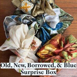 May include: Four fabric-wrapped gifts, each tied with a different patterned fabric. The fabrics are a floral print, a paisley print, a blue and green print, and a red and yellow print. The text "Old, New, Borrowed, & Blue Surprise Box" is at the bottom of the image.