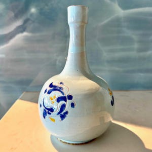 May include: A white ceramic vase with a round body and a long, thin neck. The vase is decorated with blue and yellow floral designs.