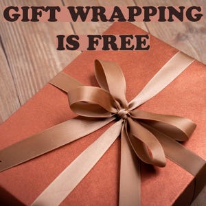 May include: A square gift box wrapped in metallic copper paper with a matching satin ribbon tied in a bow on top. The text GIFT WRAPPING IS FREE is printed in dark brown letters across the upper portion of the image, centered above the box.