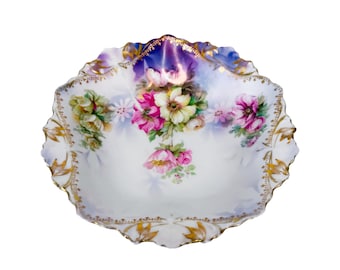May include: A white porcelain serving dish with a scalloped edge and gold trim. The dish features a hand-painted floral design in shades of pink, yellow, and green. The rim has a blue and purple gradient.