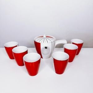 Könnte beinhalten: Ein rotes und weißes Keramik-Teeservice. Das Set umfasst eine Teekanne mit Deckel und Griff sowie sechs passende Tassen. Die Teekanne hat ein rot-weißes Design mit schwarzen Linien. Die Tassen sind rot mit weißem Innenraum.
