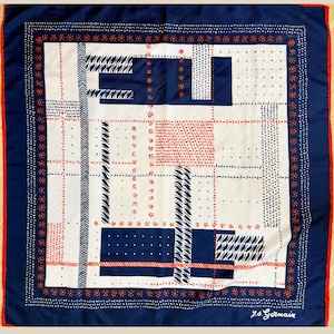May include: A square silk scarf with a geometric pattern in navy blue, white, and red. The scarf has a navy blue border with a floral design and a red edge. The design includes rectangles, lines, and floral accents. The scarf is signed "J.S. Germain".
