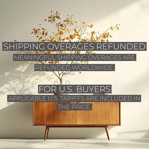 May include: A wooden cabinet with mid-century modern design, featuring a warm, natural wood finish. The cabinet has a rectangular shape with angled legs. Above the cabinet is a small vase with branches and leaves. Text on the image reads: SHIPPING OVERAGES REFUNDED.