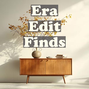 May include: A mid-century modern wooden cabinet with two doors and angled legs. A beige ceramic vase and a small stack of books sit on top. The text "Era Edit Finds" is displayed above the cabinet.