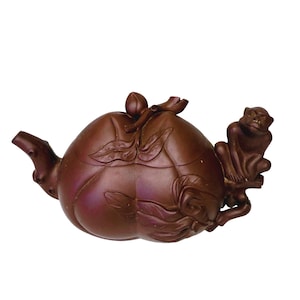 以下が含まれることがあります： 桃の形をした茶色の陶器のティーポットで、彫刻された花と葉のディテールが特徴です。小さな猿のフィギュアが側面に付いた枝に座っています。ティーポットには注ぎ口と、つぼみの形をしたハンドルが付いた蓋があります。