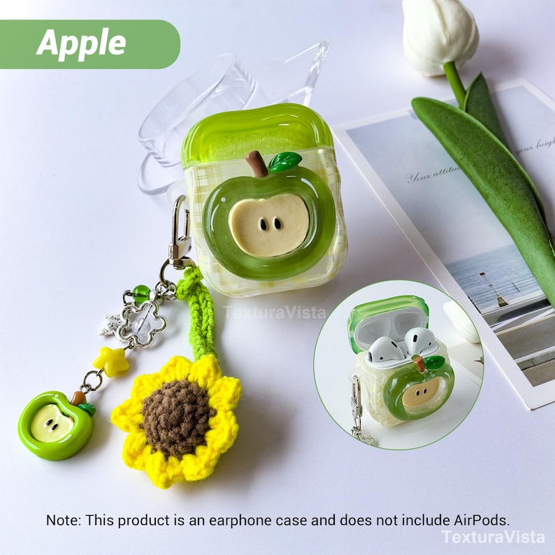 K&ouml;nnte beinhalten: Gr&uuml;nes Apfel-Ohrh&ouml;rer-Etui mit passendem Anh&auml;nger. Das Etui hat einen transparenten Deckel und ein gr&uuml;nes Apfeldesign mit beigem Kern. Ein gelber Sonnenblumen- und ein gr&uuml;ner Apfelanh&auml;nger sind angebracht. Der Text "Apple" befindet sich in einer gr&uuml;nen Box.