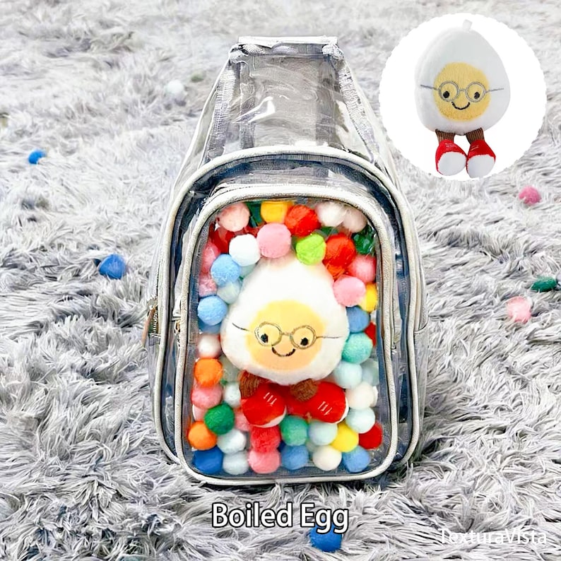 Puede incluir: Una mochila transparente con cierre de cremallera, llena de pompones de colores y un personaje de huevo cocido de peluche con gafas. La mochila tiene un peque&ntilde;o personaje de huevo de peluche adjunto.