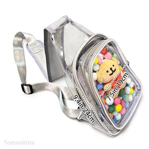 Puede incluir: Bolso bandolera transparente con correa y ribete plateados. El bolso tiene un bolsillo frontal lleno de pompones de colores y un peque&ntilde;o peluche. El bolso mide 24 cm por 19 cm.