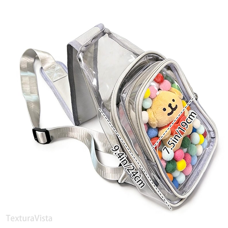 Puede incluir: Bolso bandolera transparente con correa y ribete plateados. El bolso tiene un bolsillo frontal lleno de pompones de colores y un peque&ntilde;o peluche. El bolso mide 24 cm por 19 cm.