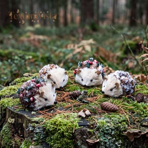 May include: Four decorative hedgehog figurines crafted with cream-colored faux fur faces and bodies covered in brown pinecone scales, accented with small red berries and green foliage. The hedgehogs are arranged on a mossy tree stump.