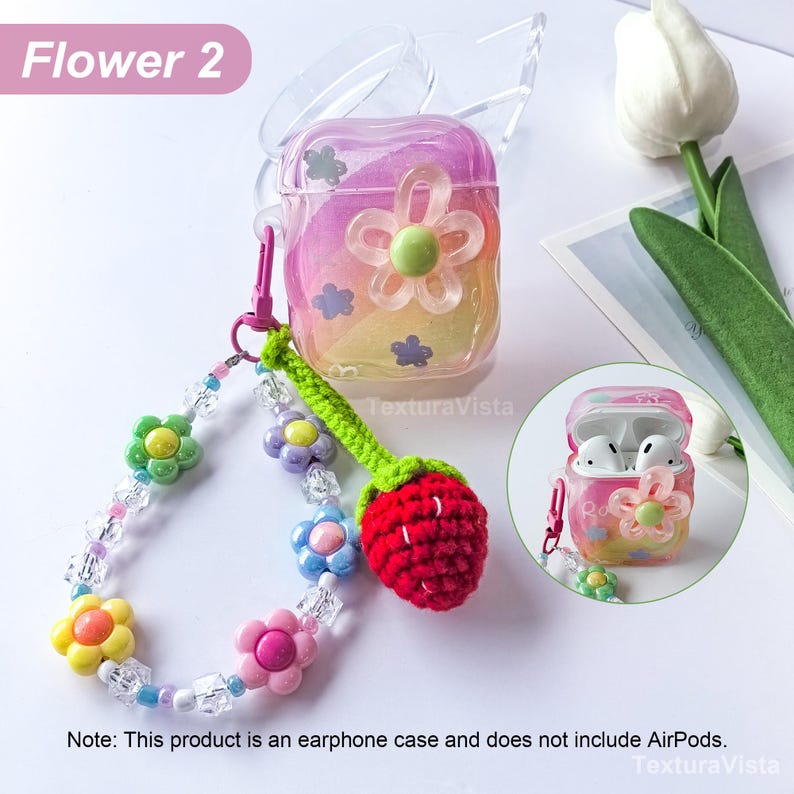 K&ouml;nnte beinhalten: Eine transparente Kopfh&ouml;rerh&uuml;lle mit Farbverlauf und Blumenmuster. Sie hat einen Perlenriemen mit Blumen- und Kristallakzenten sowie einen geh&auml;kelten Erdbeer-Anh&auml;nger. Der Text "Flower 2" ist sichtbar.