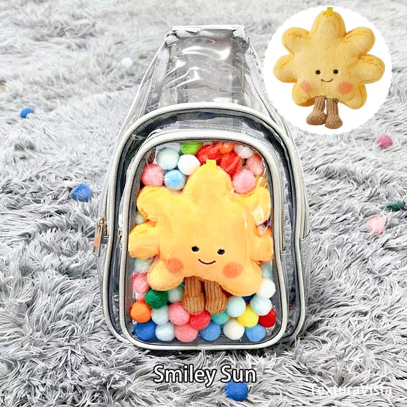 Puede incluir: Una mochila transparente con ribete plateado, llena de pompones coloridos y un sol de peluche amarillo con una cara sonriente. El texto "Smiley Sun" est&aacute; impreso en la parte inferior. Se muestra un sol de peluche separado en un c&iacute;rculo.