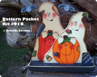 May include: A wooden craft kit featuring three ghosts holding pumpkins. The ghosts are painted white with black eyes and mouths. The pumpkins are orange with green stems and painted faces. The kit is labeled "Pattern Packet Kit #918" and "Brenda Sattley".