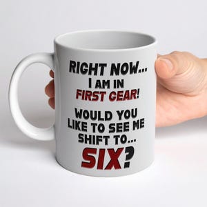 May include: White ceramic mug with black and red text. The text reads "RIGHT NOW... I AM IN FIRST GEAR! WOULD YOU LIKE TO SEE ME SHIFT TO... SIX?" The mug has a large handle and is held by a hand.