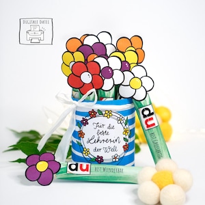 Könnte beinhalten: Ein blau-weiß gestreifter Behälter, der mit einem weißen Band gebunden ist und mit bunten Papierblumen gefüllt ist. Der Behälter trägt den Text "Für die beste Lehrerin der Welt". Zwei grüne Schokoriegel mit dem Wort "du" und dem Text "Bist Wunderbar" sind ebenfalls zu sehen.