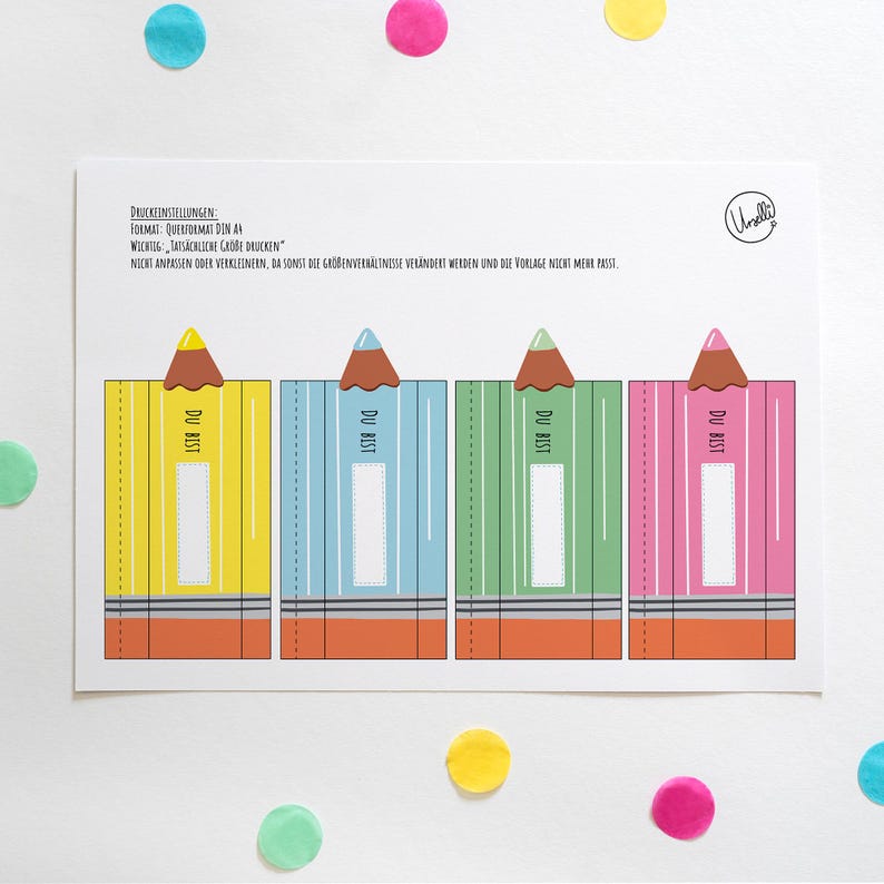 May include: A white card featuring four colorful pencil-shaped designs. Each pencil is a different color: yellow, blue, green, and pink. The pencils have brown tips and the text "DU BIST". Colorful confetti dots the background.