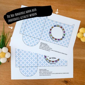May include: Two white paper templates for a box sleeve featuring a light blue geometric pattern of overlapping circles. Each template includes a circular frame decorated with small colorful hearts and German text instructions for printing on A4 paper.