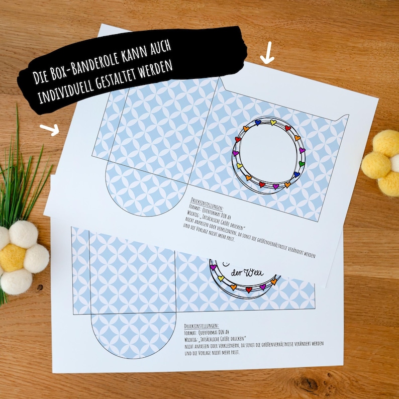 May include: Two white paper templates for a box sleeve featuring a light blue geometric pattern of overlapping circles. Each template includes a circular frame decorated with small colorful hearts and German text instructions for printing on A4 paper.