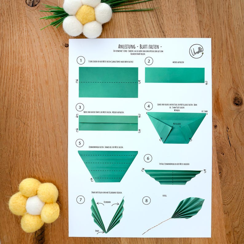 May include: A white instructional sheet titled ANLEITUNG - BLATT FALTEN featuring eight numbered steps with green paper diagrams illustrating how to fold a leaf shape. The document includes text instructions and a logo in the top right corner.