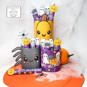 May include: A collection of Halloween-themed paper crafts. The crafts include a large yellow pumpkin, a gray spider, and a purple container with ghosts, spiders, and skeletons. The phrase "HAPPY HALLOWEEN" is printed on a small orange item. The image also includes a small orange pumpkin.