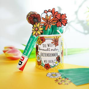 May include: A yellow container with a floral design and the text "DIE WELT braucht mehr ERZIEHERINNEN wie DICH" holds paper flowers. A green and white object with the text "bist wundervoll" leans against the container. The background is yellow.