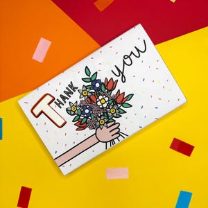 Puede incluir: Una tarjeta blanca con las palabras "Thank you" y un ramo de flores. La tarjeta tiene un patrón de confeti colorido y está colocada sobre un fondo amarillo, naranja y rojo con confeti disperso.