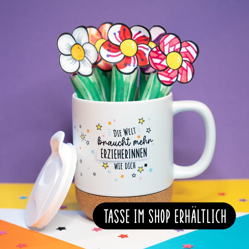 May include: A white ceramic mug with a cork base and a white lid, filled with paper flowers. The mug features the German text "DIE WELT braucht mehr ERZIEHERINNEN WIE DICH" surrounded by small colorful stars. A black label reads "TASSE IM SHOP ERH&Auml;LTLICH".
