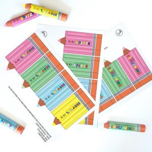 May include: A collection of colorful pencil-shaped cards and crayons. The cards feature a pencil design with the text "DU BIST 1.KLASSE" and "SPITZE". The crayons are cylindrical with the text "ENDLICH SCHULKIND". The color palette includes pink, green, blue, and yellow.
