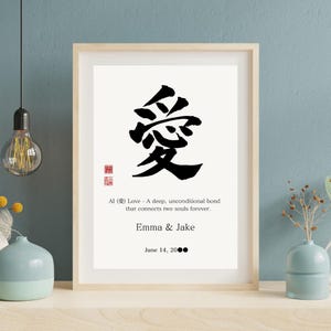 以下が含まれることがあります： 黒い日本の愛の書道シンボルが描かれた額入りのプリント。下には英語のテキストがあります。テキストは「Al（愛）Love-2つの魂を永遠に繋ぐ、深く無条件の絆」と書かれています。「Emma＆Jake」という名前と日付も含まれています。