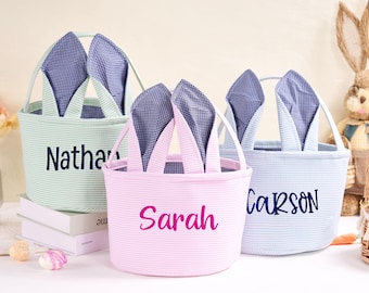Peut inclure: Trois paniers de Pâques de couleur pastel avec des oreilles de lapin. Les paniers sont en tissu et ont un motif rayé. Les paniers sont personnalisés avec les noms "Nathan", "Sarah" et "Carson".