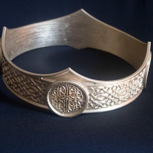 May include: A silver crown featuring a Celtic knot design and a central circular medallion with a four-leaf clover pattern.