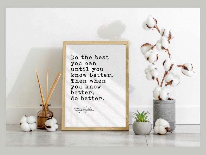 May include: A framed print with the quote 'Do the best you can until you know better. Then when you know better, do better.' in a black, typewriter-style font. The print is in a light wooden frame and is displayed with a vase of cotton stems, a small potted plant, and decorative cotton balls.