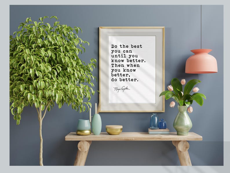 May include: A framed print with the quote "Do the best you can until you know better. Then when you know better, do better." is displayed above a wooden console table. The table holds decorative vases, bowls, and a small plant arrangement. A large green plant is on the left.