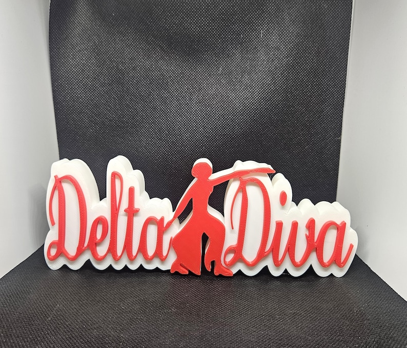 May include: White and red 3D sign with the words "Delta Diva" and a red silhouette of a woman dancing.
