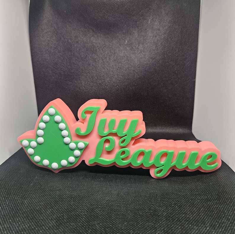 May include: A pink and green 3D sign that says "Ivy League" with a green leaf with white dots on the left side.