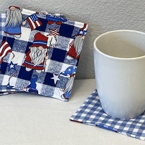 May include: Set of four fabric coasters featuring a blue and white gingham pattern with a red, white, and blue gnome design. The coasters are perfect for protecting surfaces from heat and spills.
