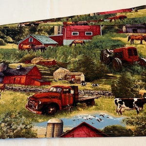May include: A stack of farm-themed placemats. The placemats feature a rural landscape with red barns, tractors, trucks, horses, and cows. The color palette includes shades of green, red, brown, and white.