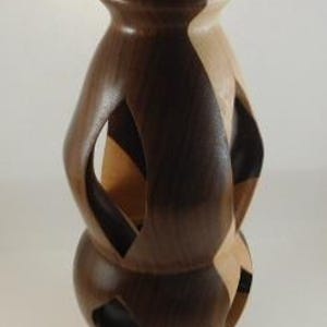 May include: A handcrafted wooden sculpture with a geometric design. The sculpture features alternating sections of dark brown and light tan wood. It has a rounded base, a central bulbous section with cut-out shapes, and a conical top.