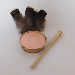 May include: A wooden turkey call with a copper soundboard and a wooden striker. The call is accompanied by a cluster of brown and black feathers. The call is designed to mimic the sounds of wild turkeys.