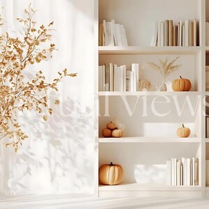 Op de afbeelding: Een witte boekenkast met meerdere planken vol boeken. De planken zijn versierd met gedroogde bloemen en kleine pompoenen. De boekenkast staat tegen een witte muur met een transparant wit gordijn op de achtergrond.